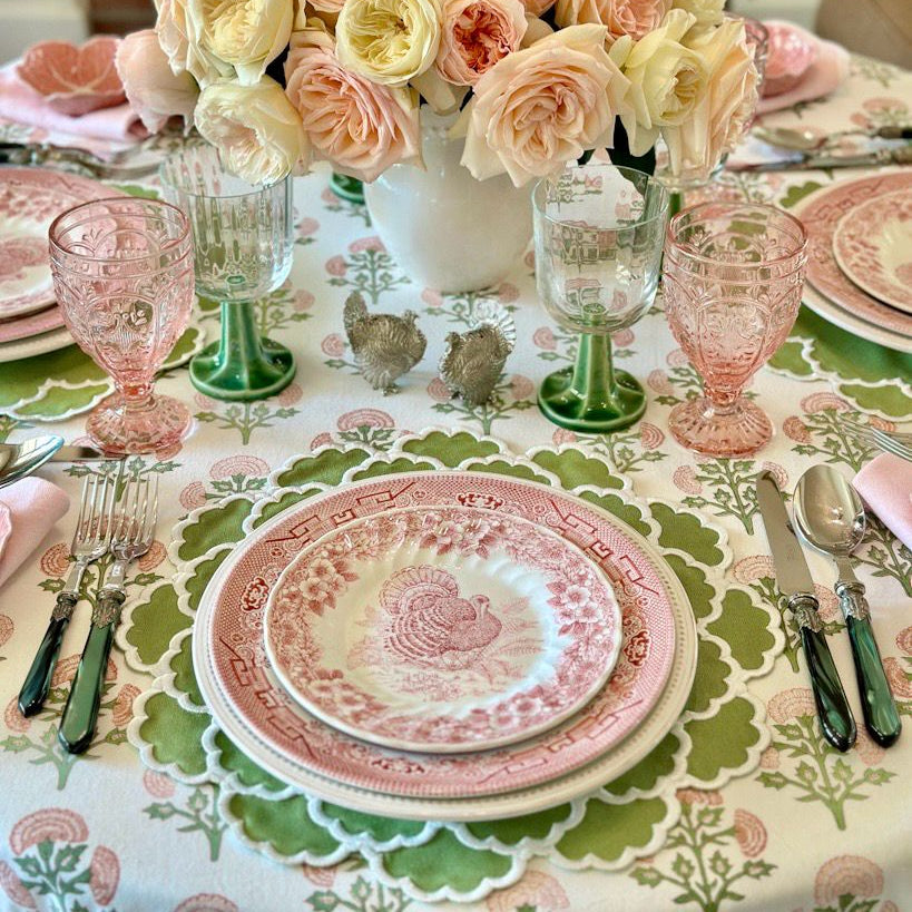Elegant table setting with floral centerpiece, pink and green glassware, and patterned tablecloth.
