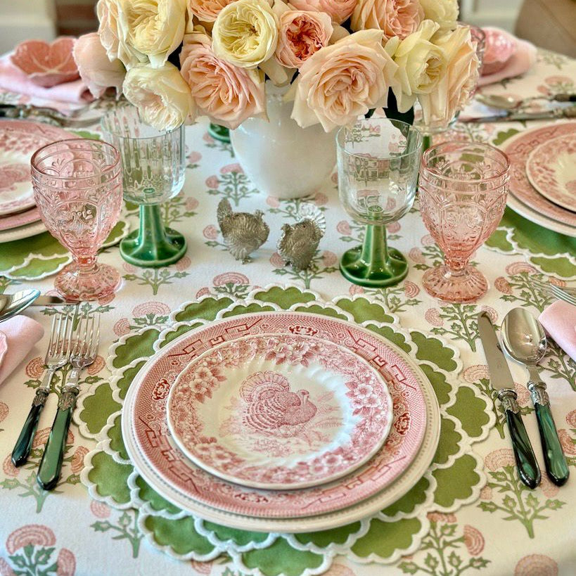 Elegant table setting with floral centerpiece, pink and green glassware, and patterned tablecloth.