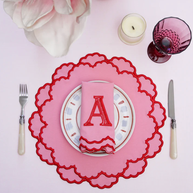 Dining table setting with pink placemat, plate, and napkin with letter 'A'.