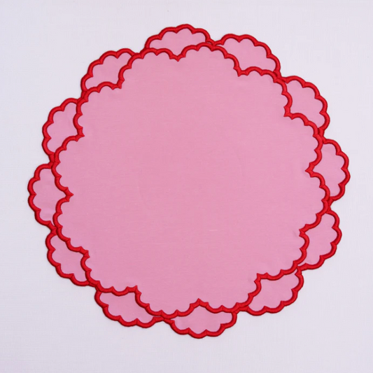 Pink scalloped placemat with red trim on a white background