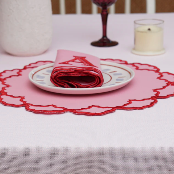 Table setting with a pink doily, plate, and folded napkin on a white tablecloth.