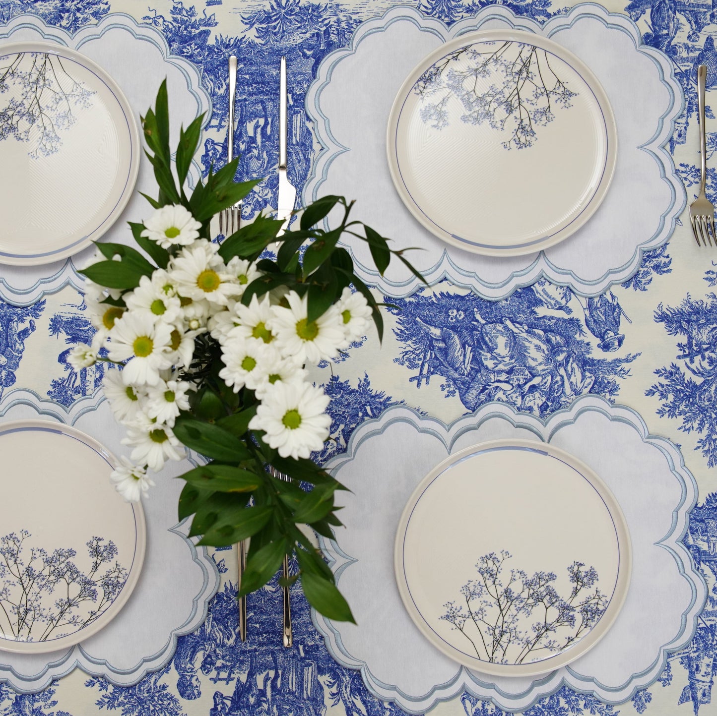 Table setting with blue and white floral tablecloth, plates, and flowers.