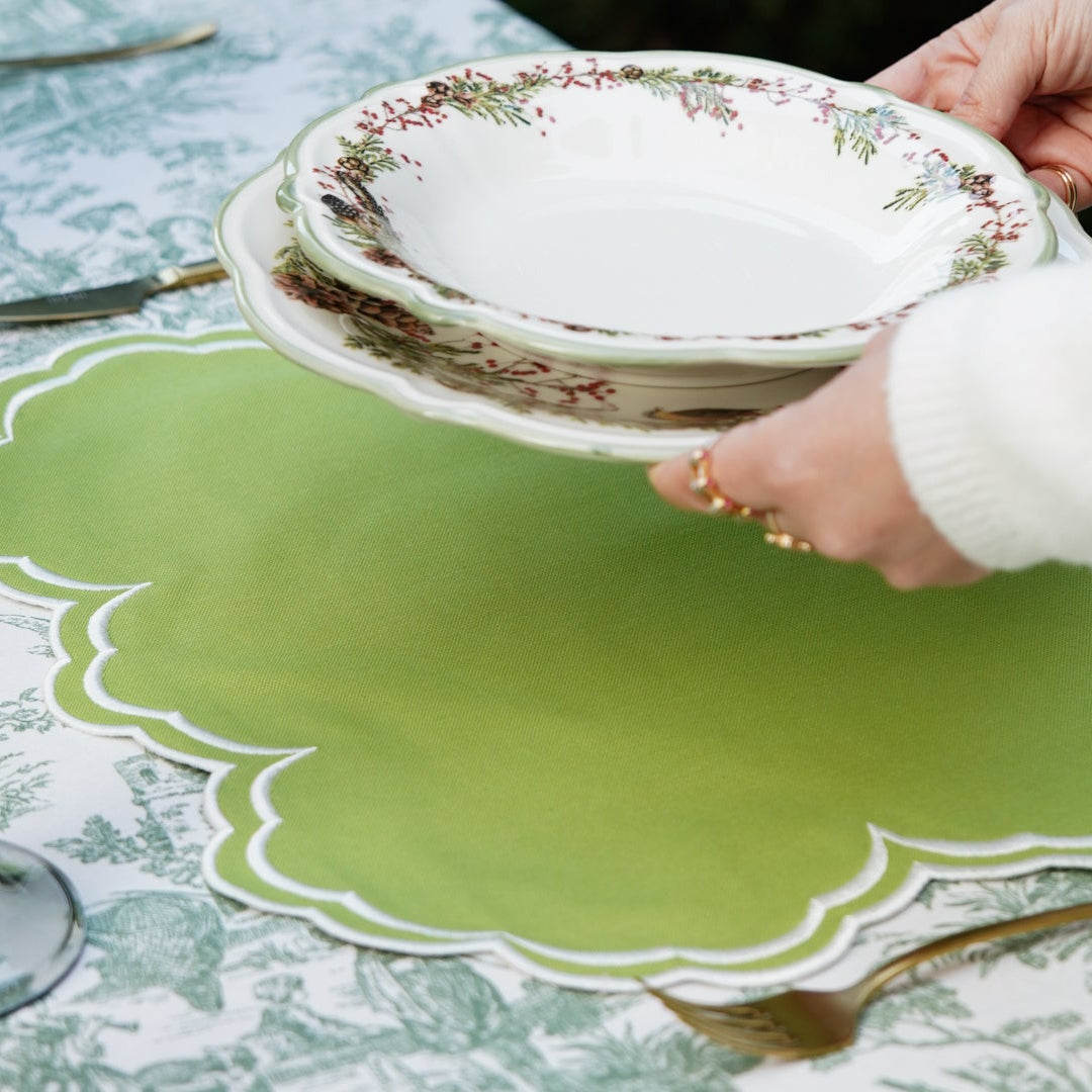Person placing a stack of plates on a green placemat at a table.