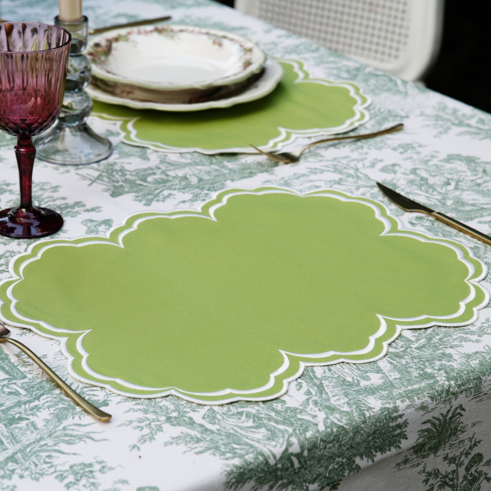Table setting with green placemats and purple glasses on a patterned tablecloth.