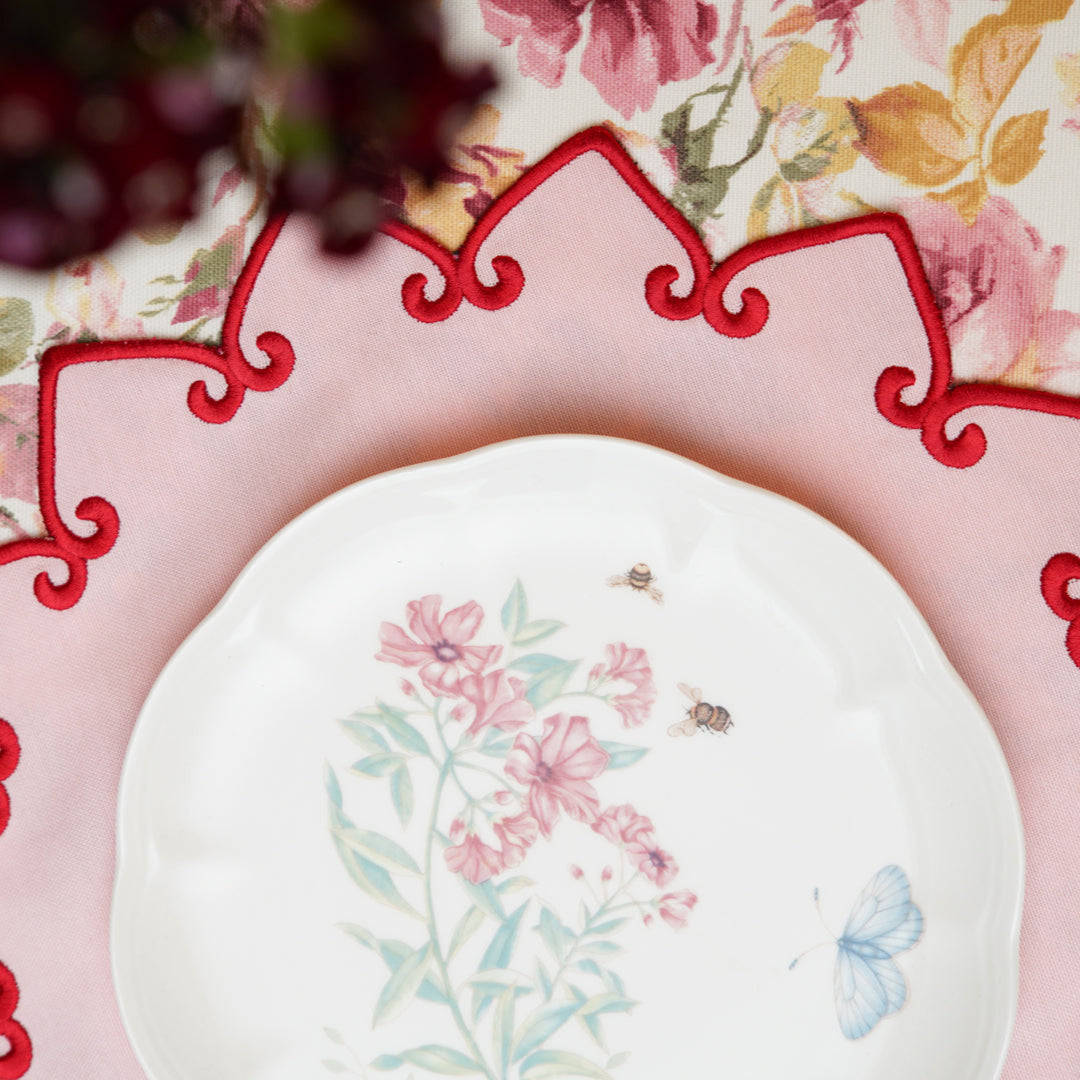 Floral-patterned plate on a decorative pink charger with a floral tablecloth background.
