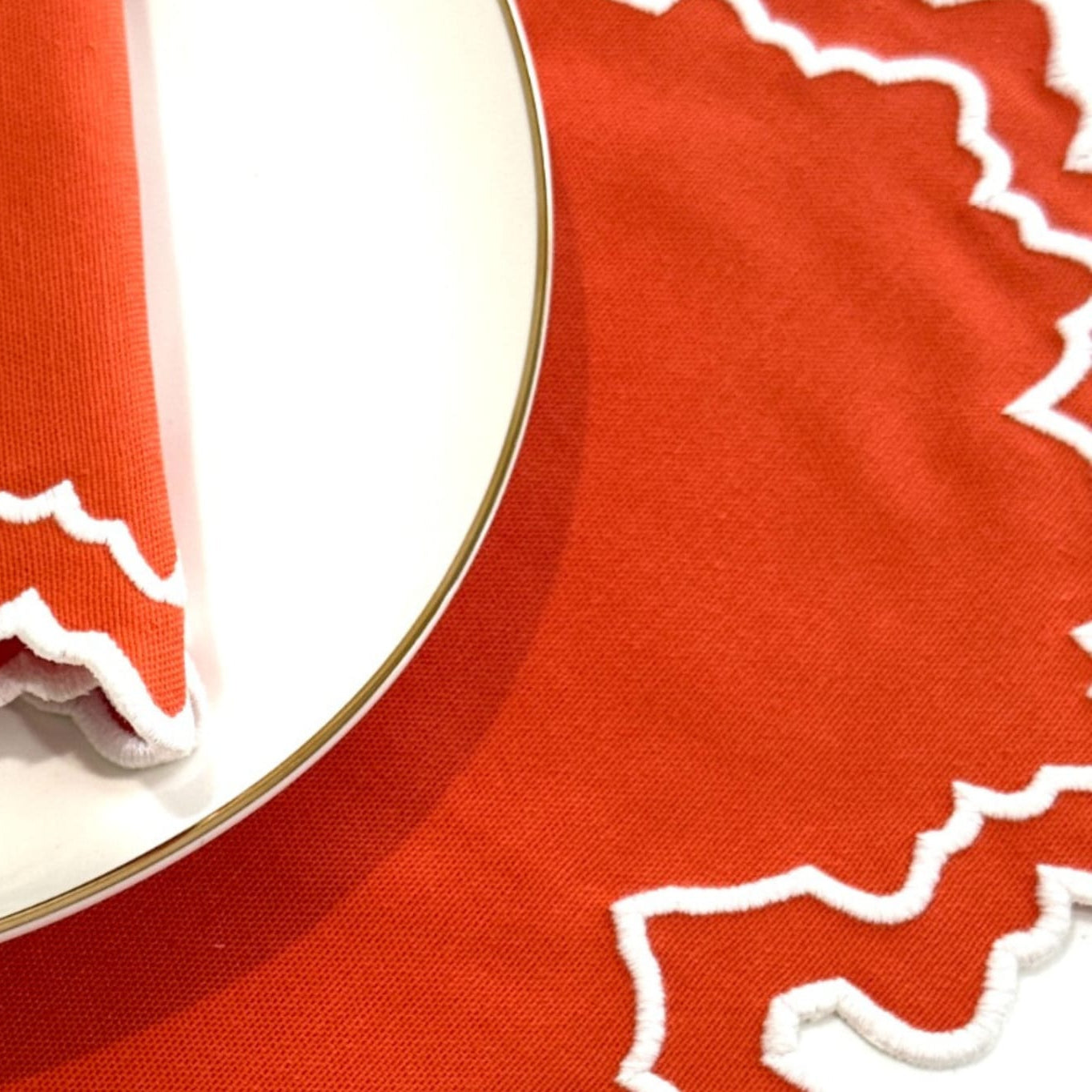 White plate with wavy white trim on a red tablecloth.