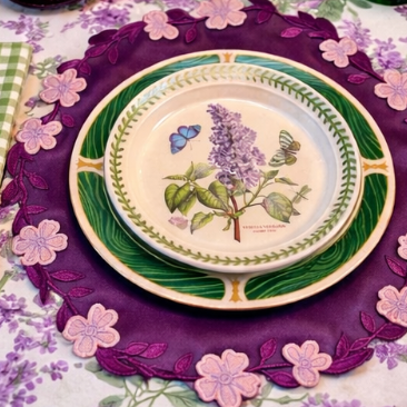 Decorative table setting with a floral tablecloth, purple charger plate, and ceramic plate with botanical design.
