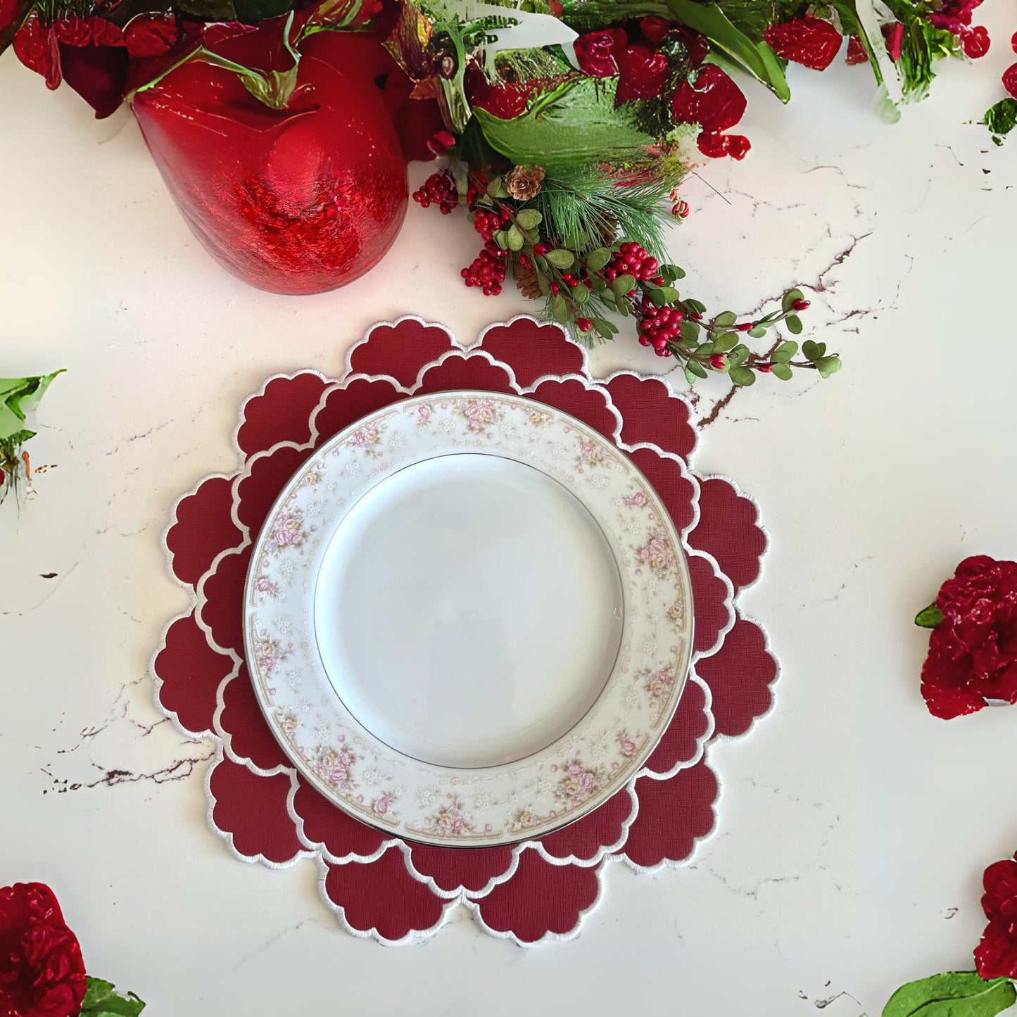 A red faux leather placemat with a round design, displayed on a white surface, with red flowers around it.