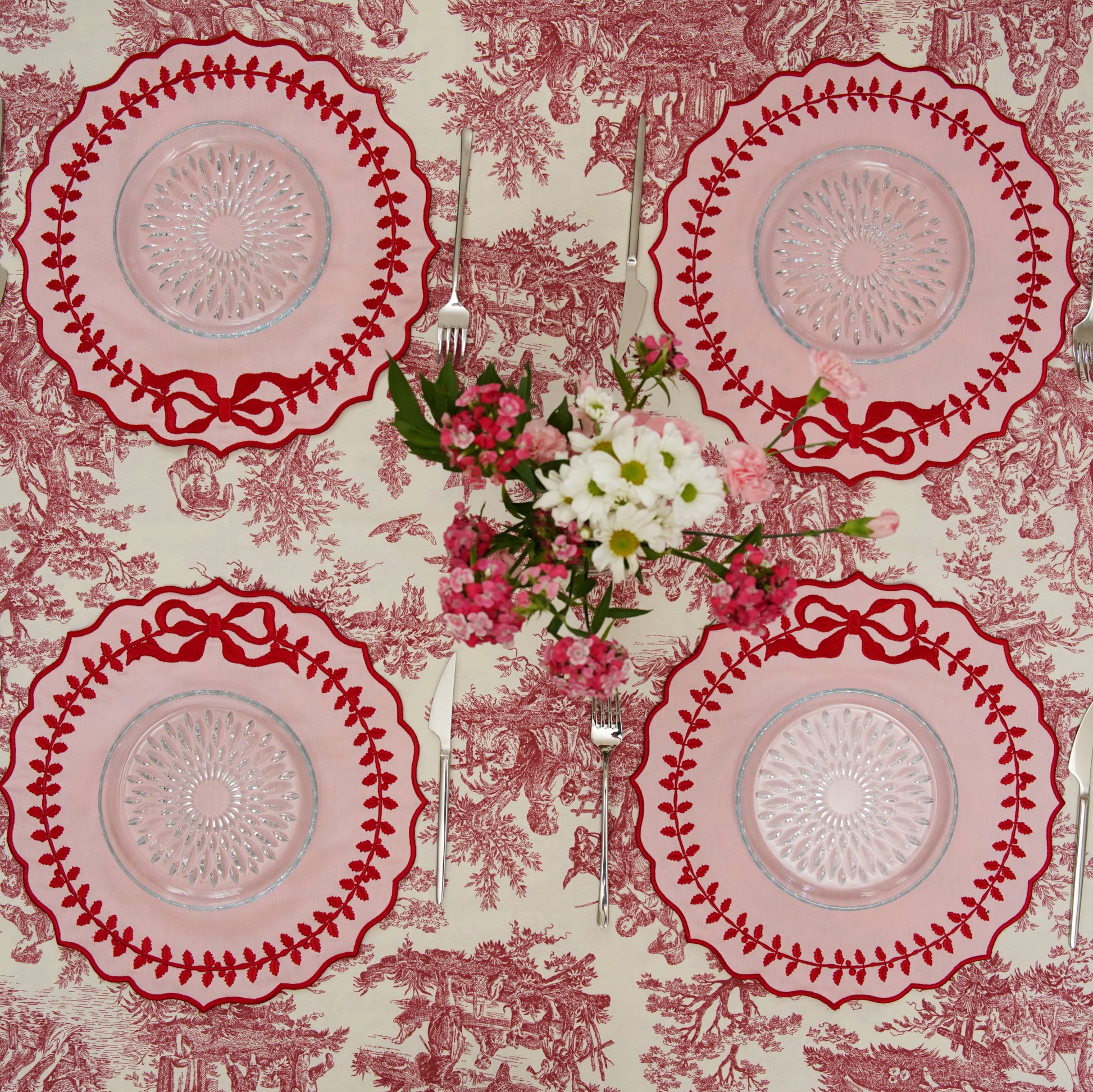 Four red and white patterned plates on a matching tablecloth with flowers.