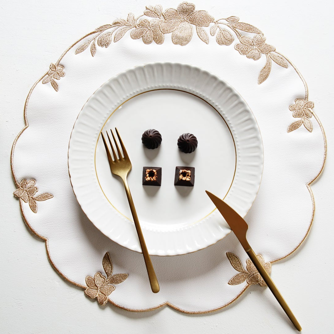 Decorative table setting with white plates, gold cutlery, and small desserts on a white background.