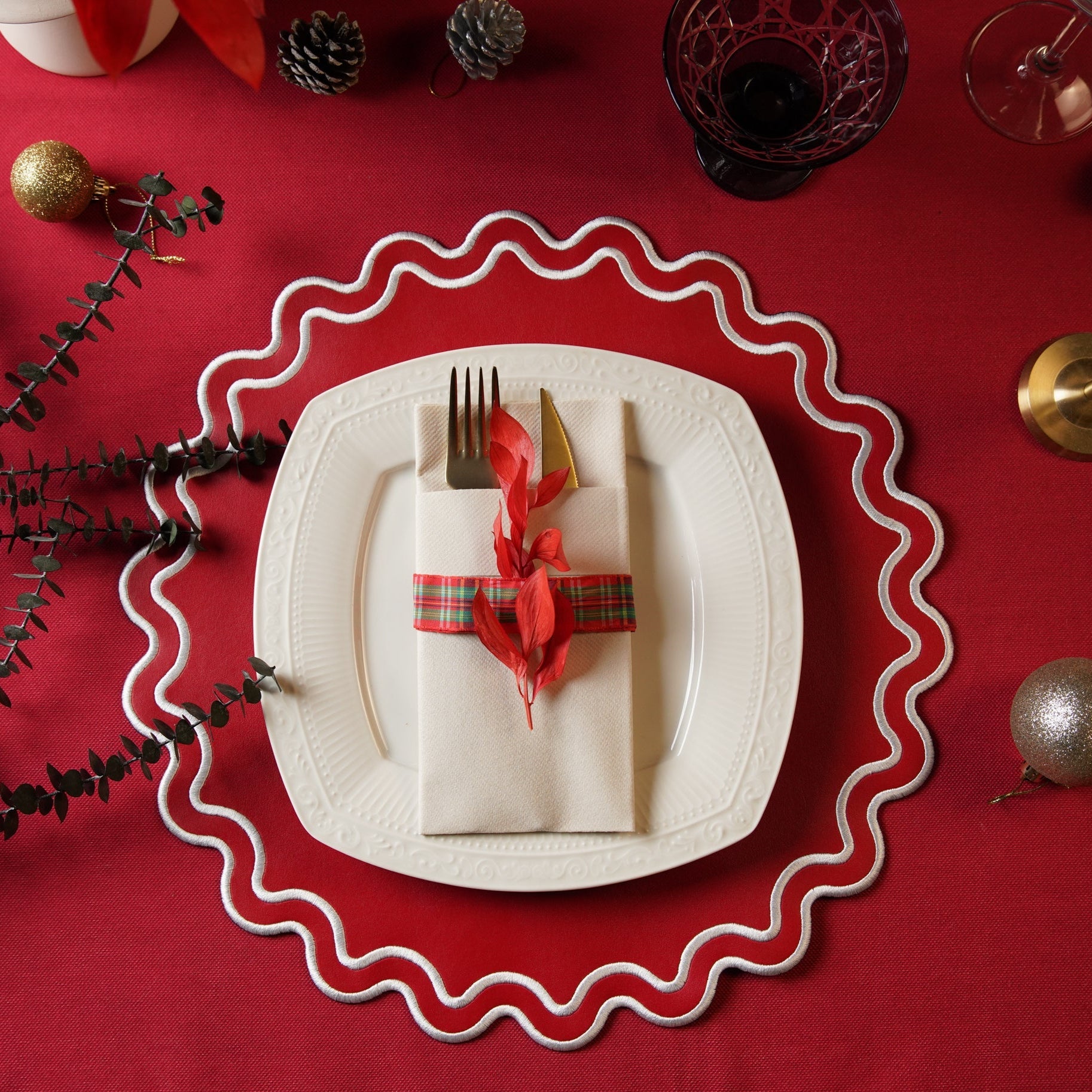 Christmas-themed table setting with a white plate, red napkin, and decorative elements on a red background.