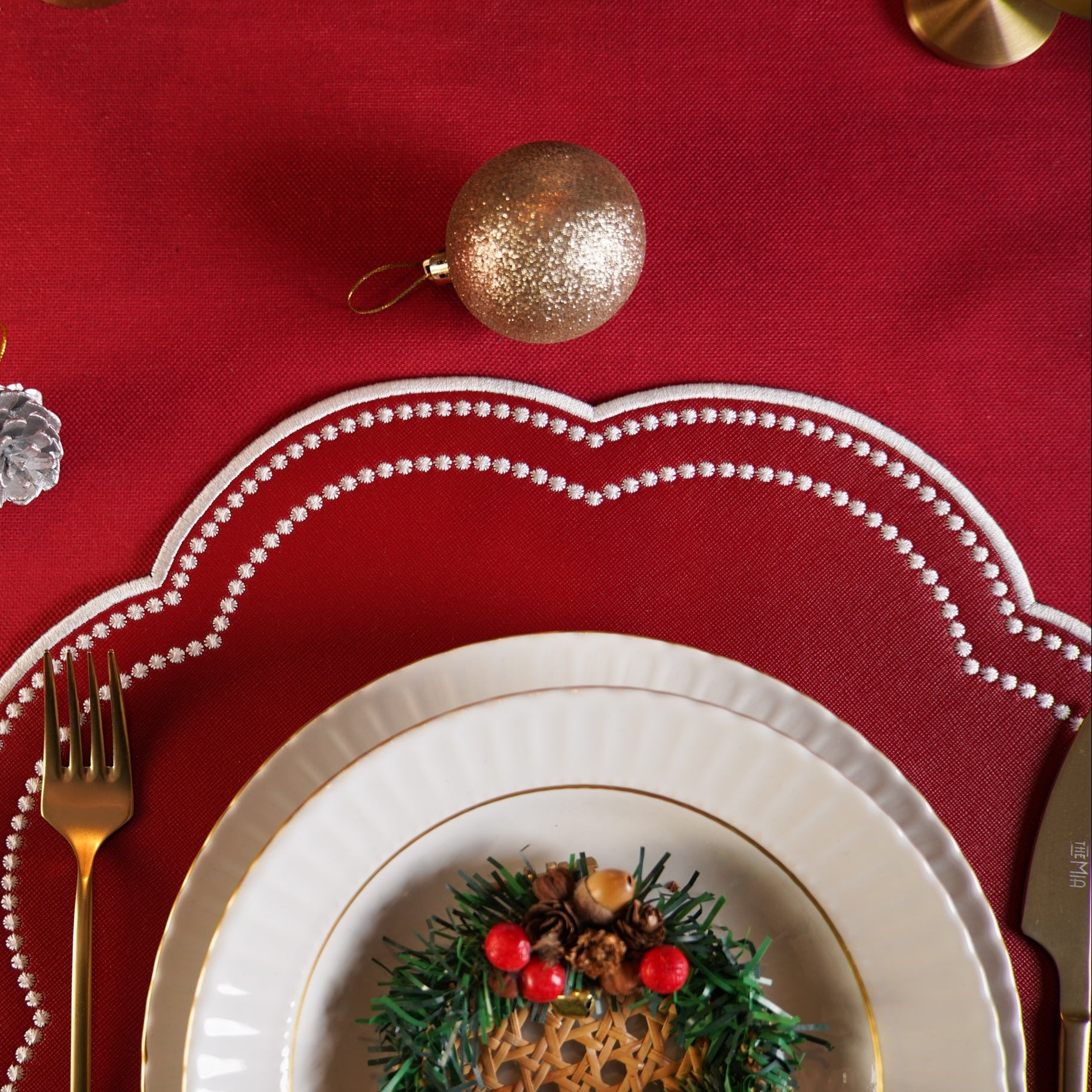 Christmas-themed table setting with red tablecloth, white plates, gold cutlery, and decorative elements.