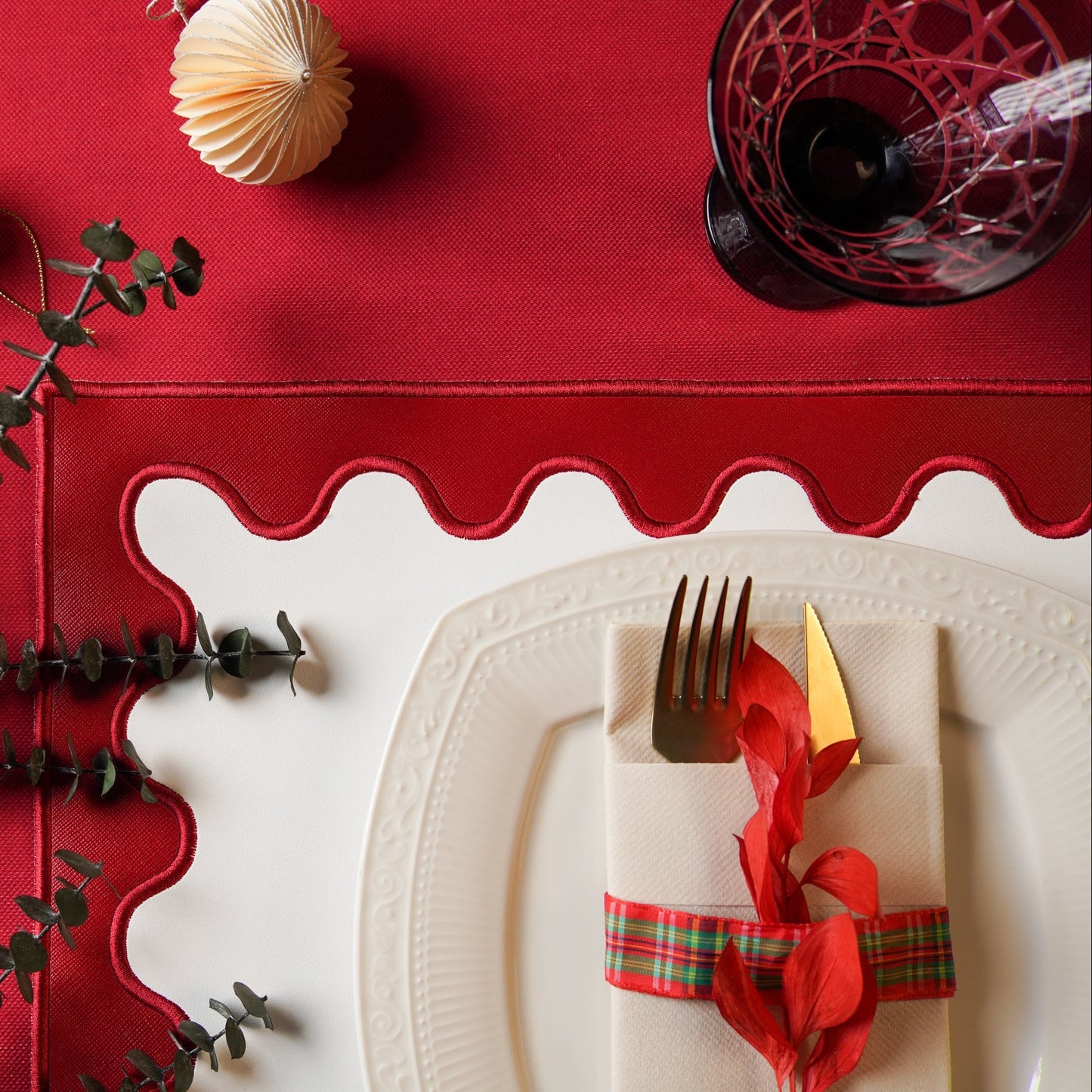 Red table runner with scalloped edge on a white tablecloth, featuring a place setting with a fork, knife, and decorative napkin.