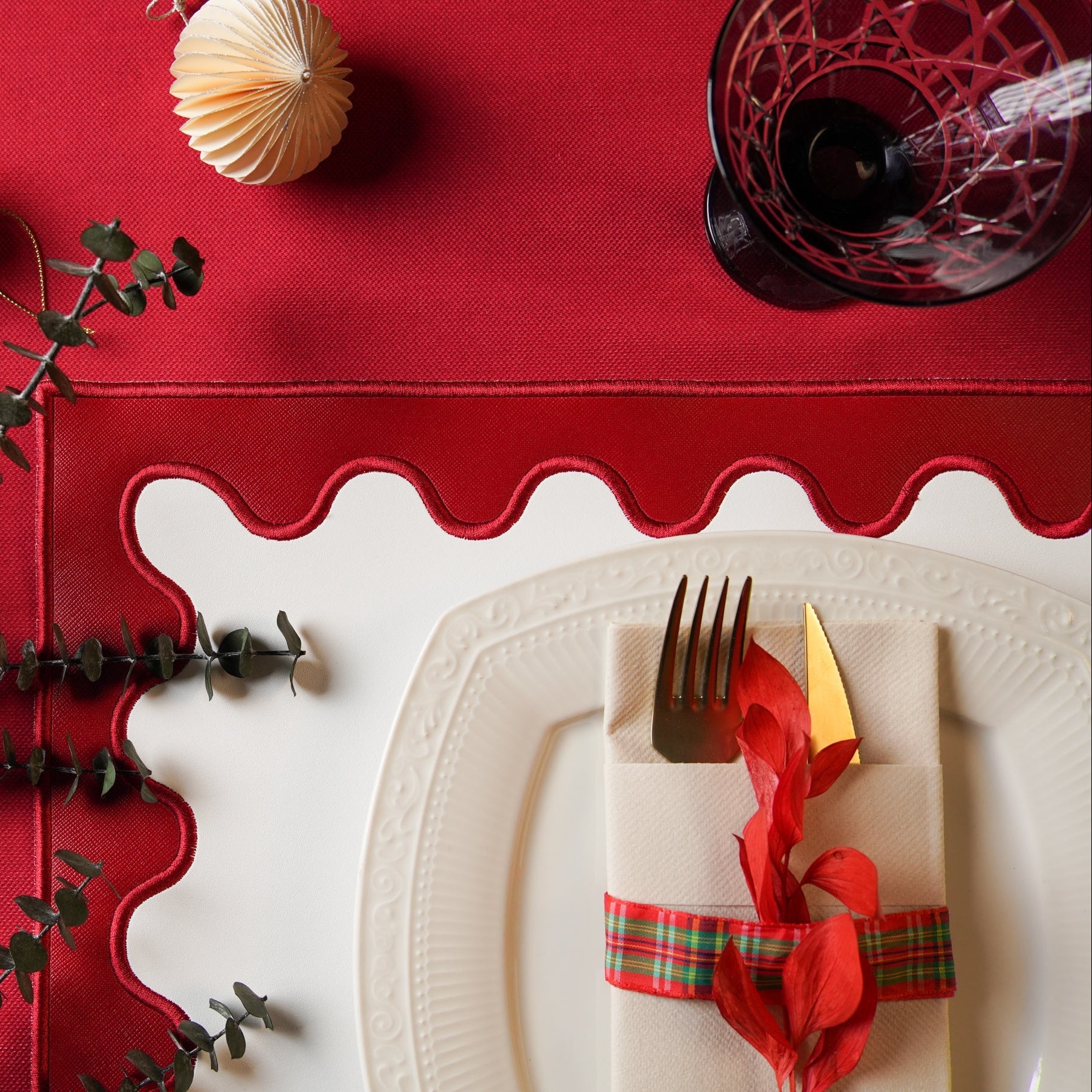 Red table runner with scalloped edge on a white tablecloth, featuring a place setting with a fork, knife, and decorative napkin.