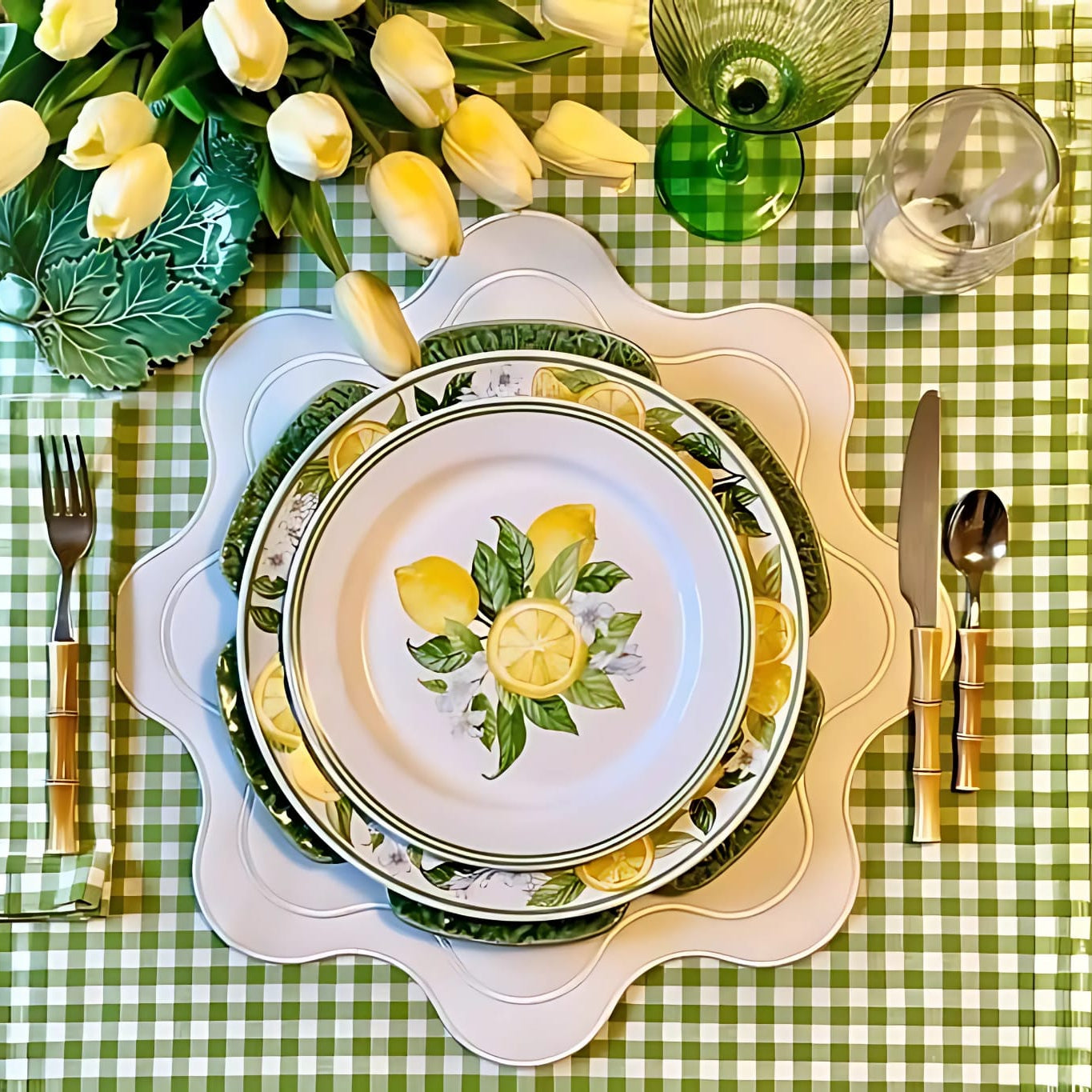 A white faux leather placemat with a dining setting on top, including a plate with a lemon and olive branch design, cutlery, and a green checkered tablecloth.