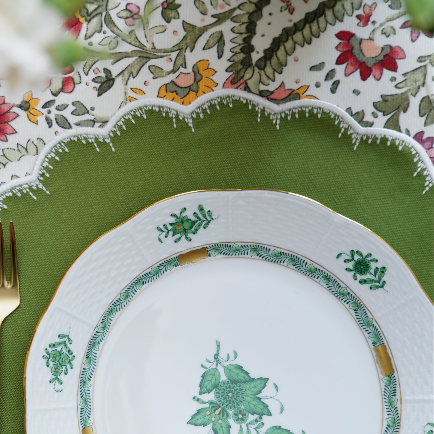 A set of elegantly embroidered placemats with a green border and floral patterns, displayed on a dining table with dishes and cutlery.
