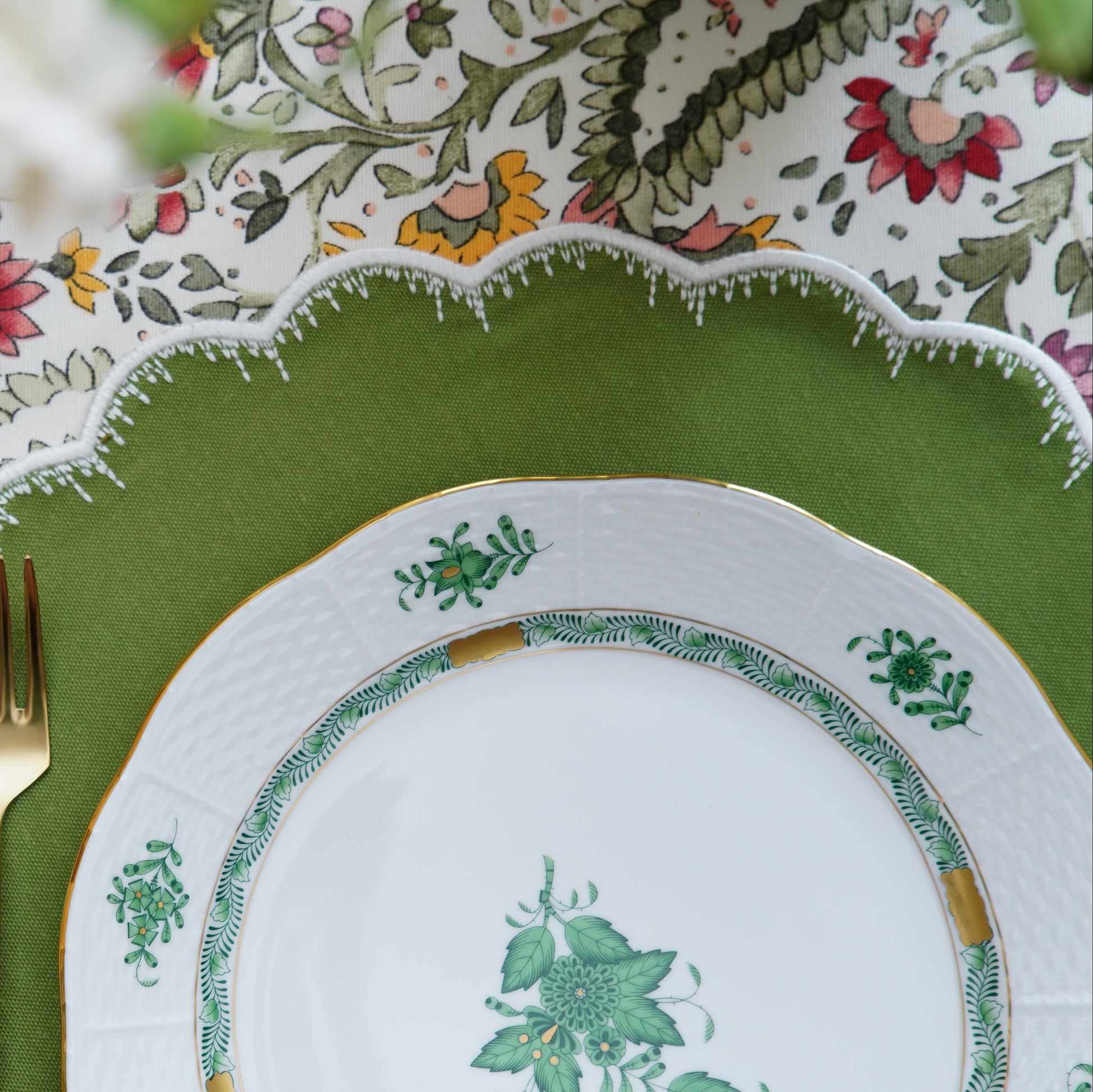 A set of elegantly embroidered placemats with a green border and floral patterns, displayed on a dining table with dishes and cutlery.