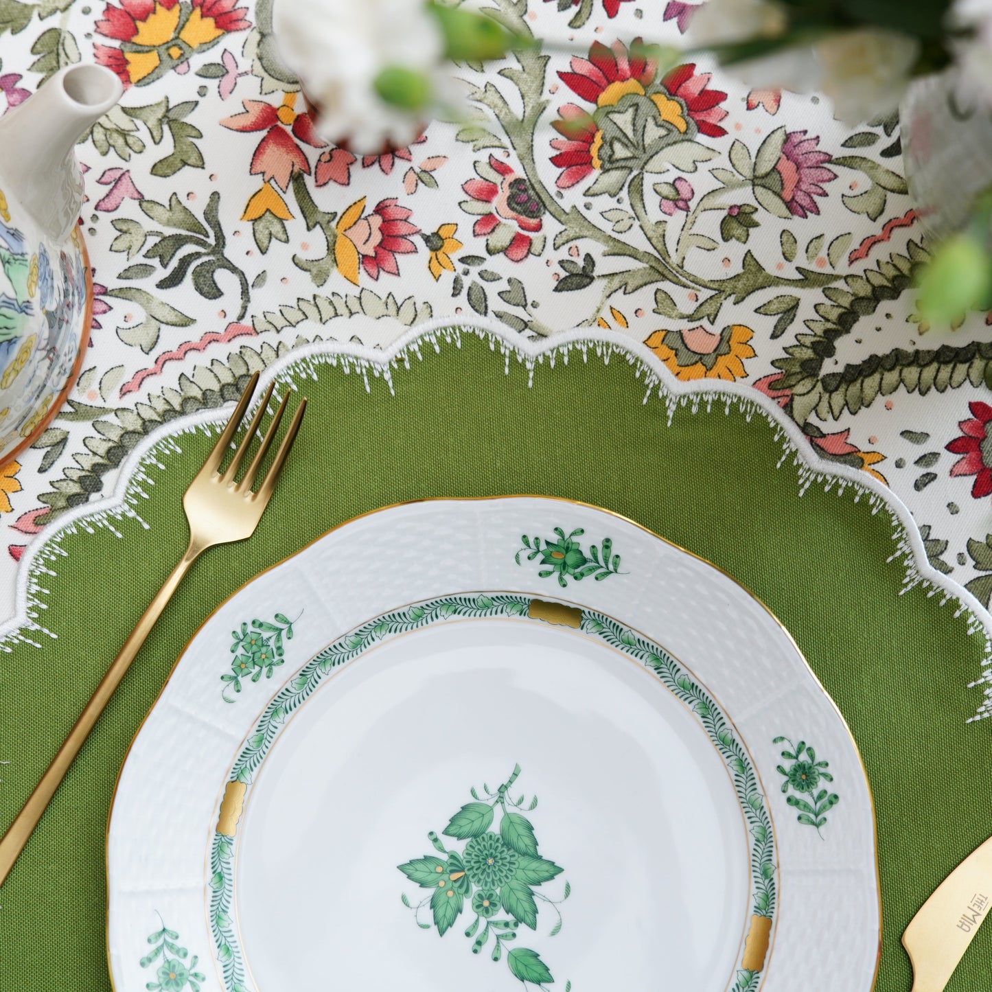 Decorative table setting with a green plate, gold fork, and floral-patterned tablecloth.