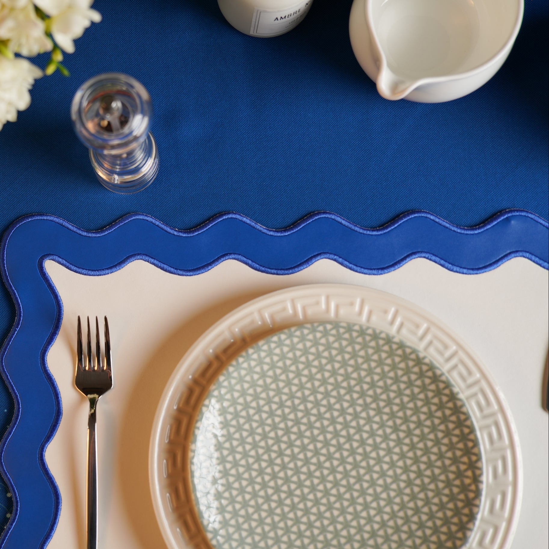 Decorative table setting with a blue placemat, white plate with geometric pattern, and silver fork.