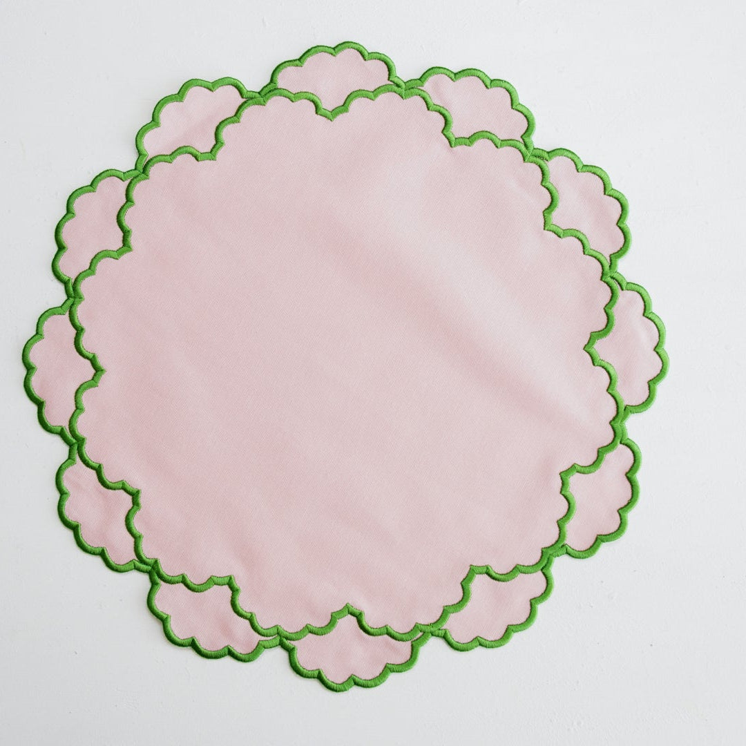 Round pink placemat with green scalloped edge on a white background