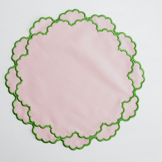 Round pink placemat with green scalloped edge on a white background