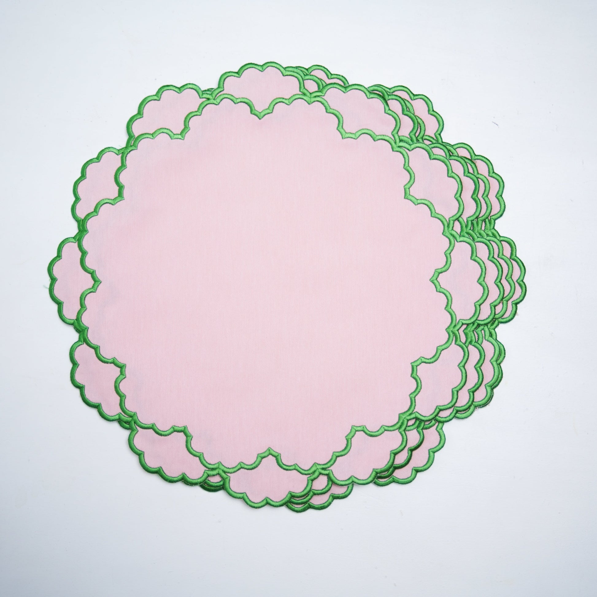 Set of pink paper doilies with green scalloped edges on a light gray background