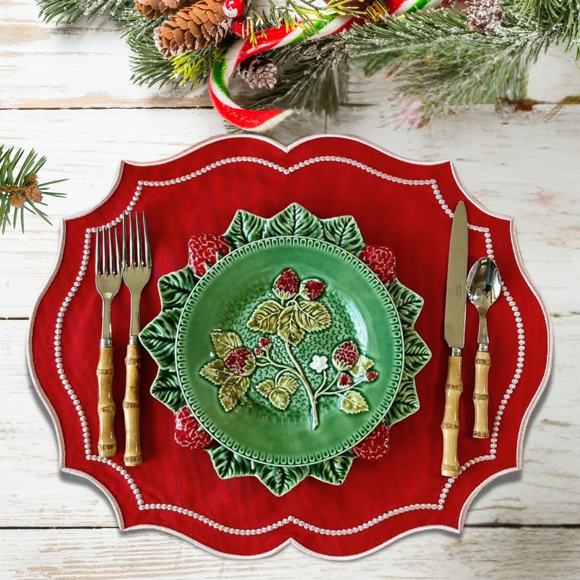 A set of crimson red embroidered fabric placemats on a dining table, surrounded by festive decorations including pine cones and Christmas-themed tableware.