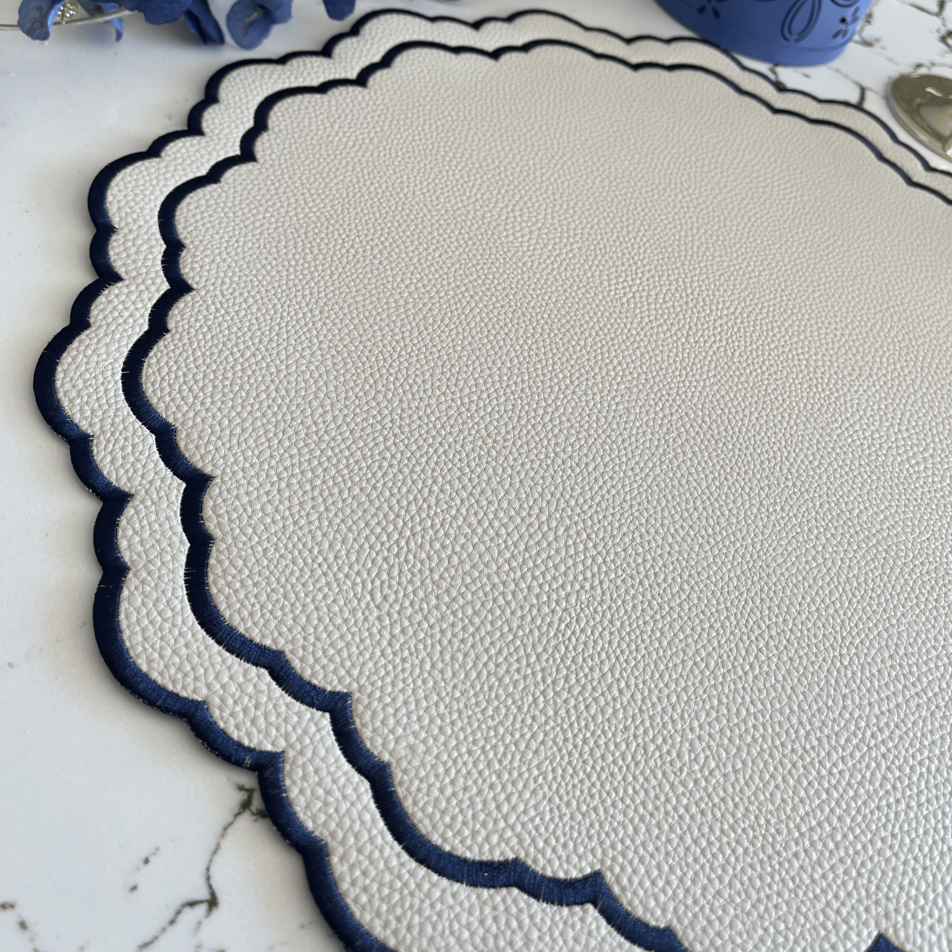 Round white placemat with blue scalloped edge on a marble surface