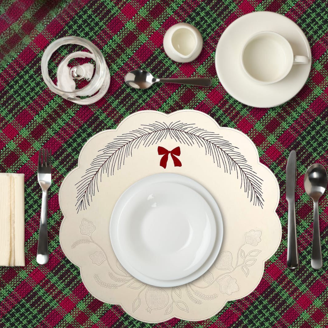 Christmas table setting with red and green plaid tablecloth, white plates, and decorative placemats.