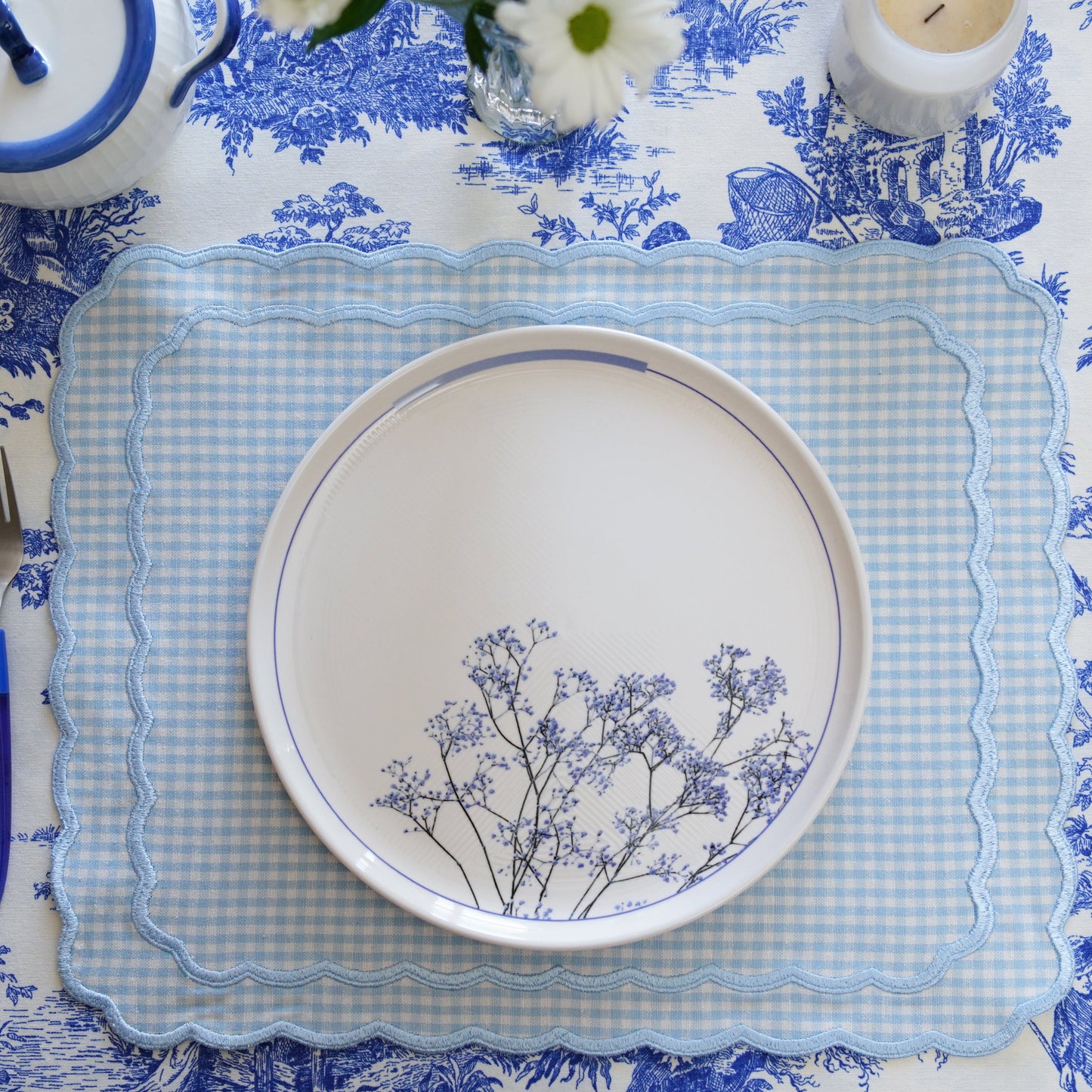 Table setting with blue and white floral patterned tablecloth, plates, and cutlery.