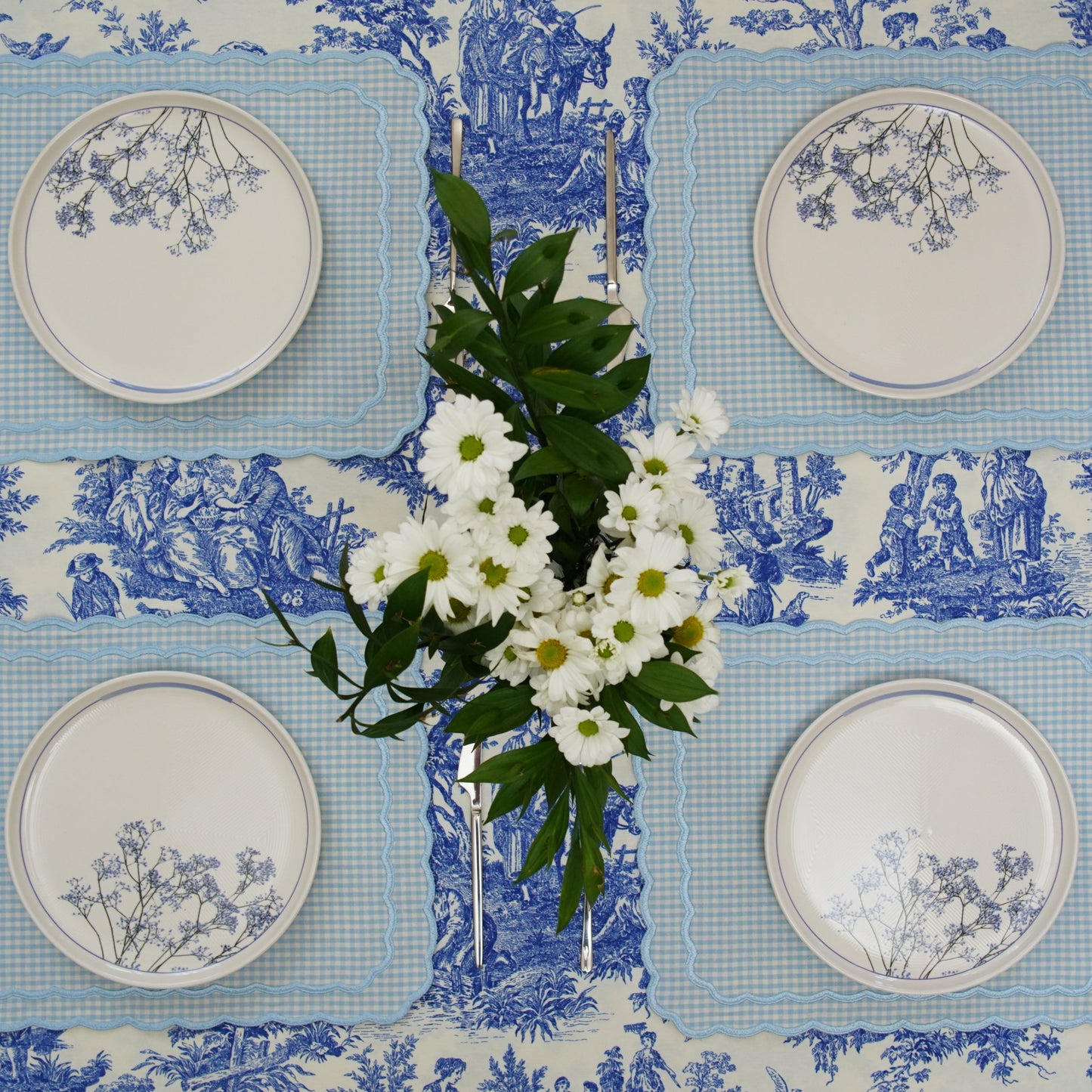 A set of blue and white floral patterned placemats displayed on a table with plates and a floral centerpiece.