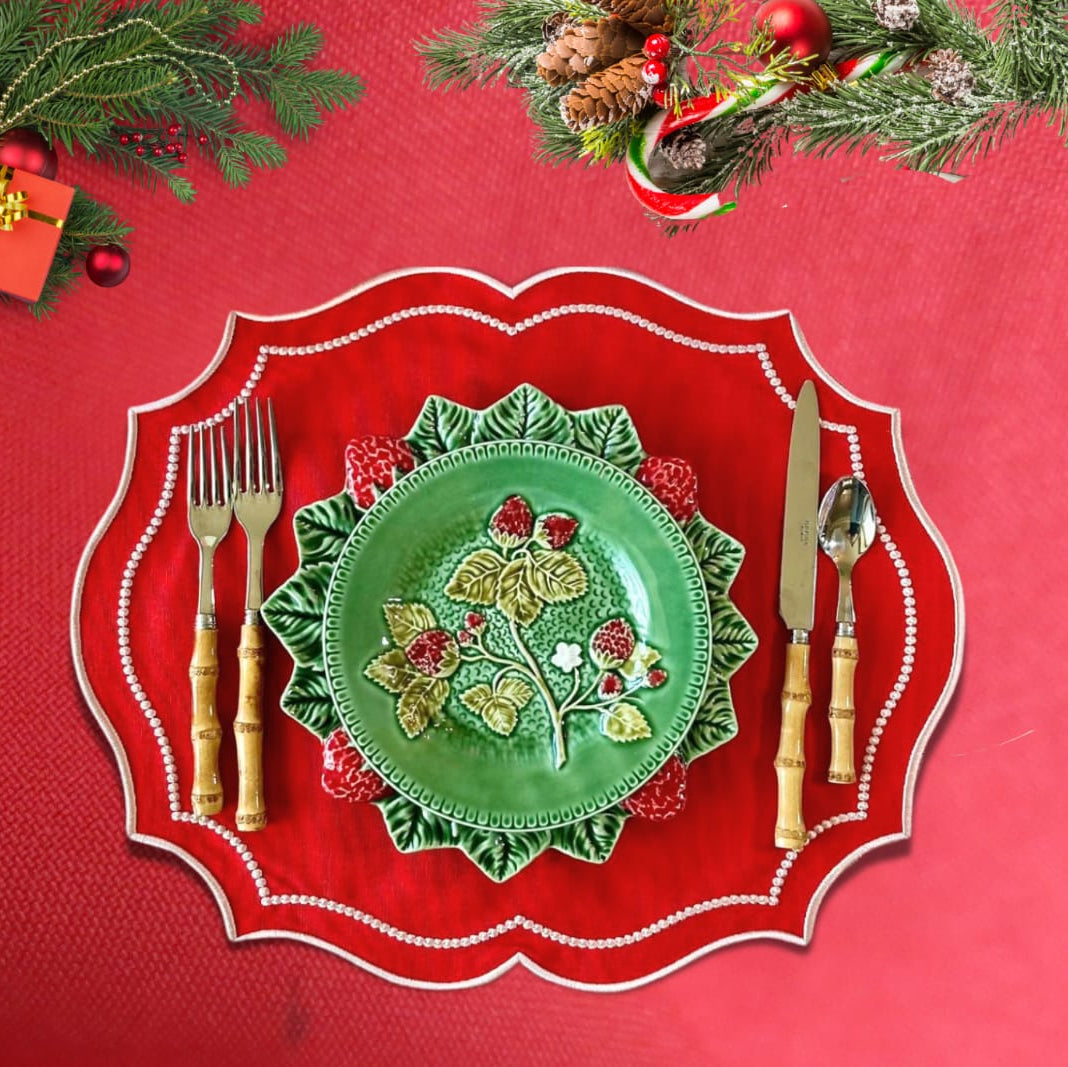 Decorative green plate with floral design on a red plate with cutlery, surrounded by Christmas decorations.
