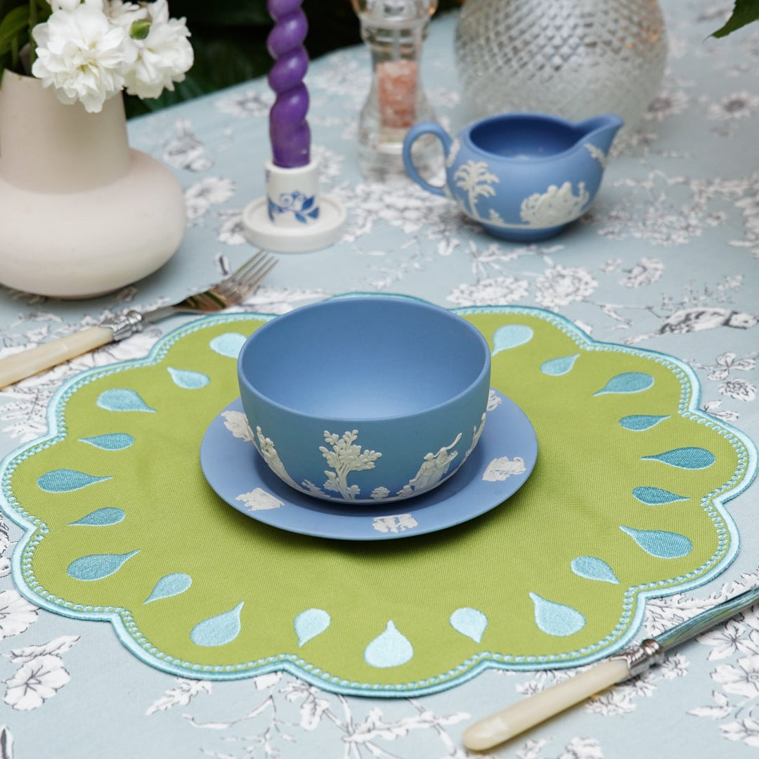 Decorative table setting with blue and greenware on a floral tablecloth.