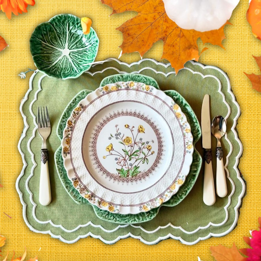 A set of green embroidered placemats on a table, with decorative elements including a white plate, silver cutlery, and autumn-themed decorations.