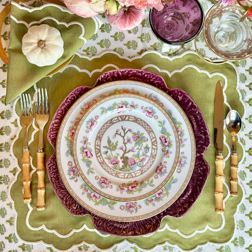 Decorative table setting with floral centerpiece, patterned plates, and cutlery on a green placemat.
