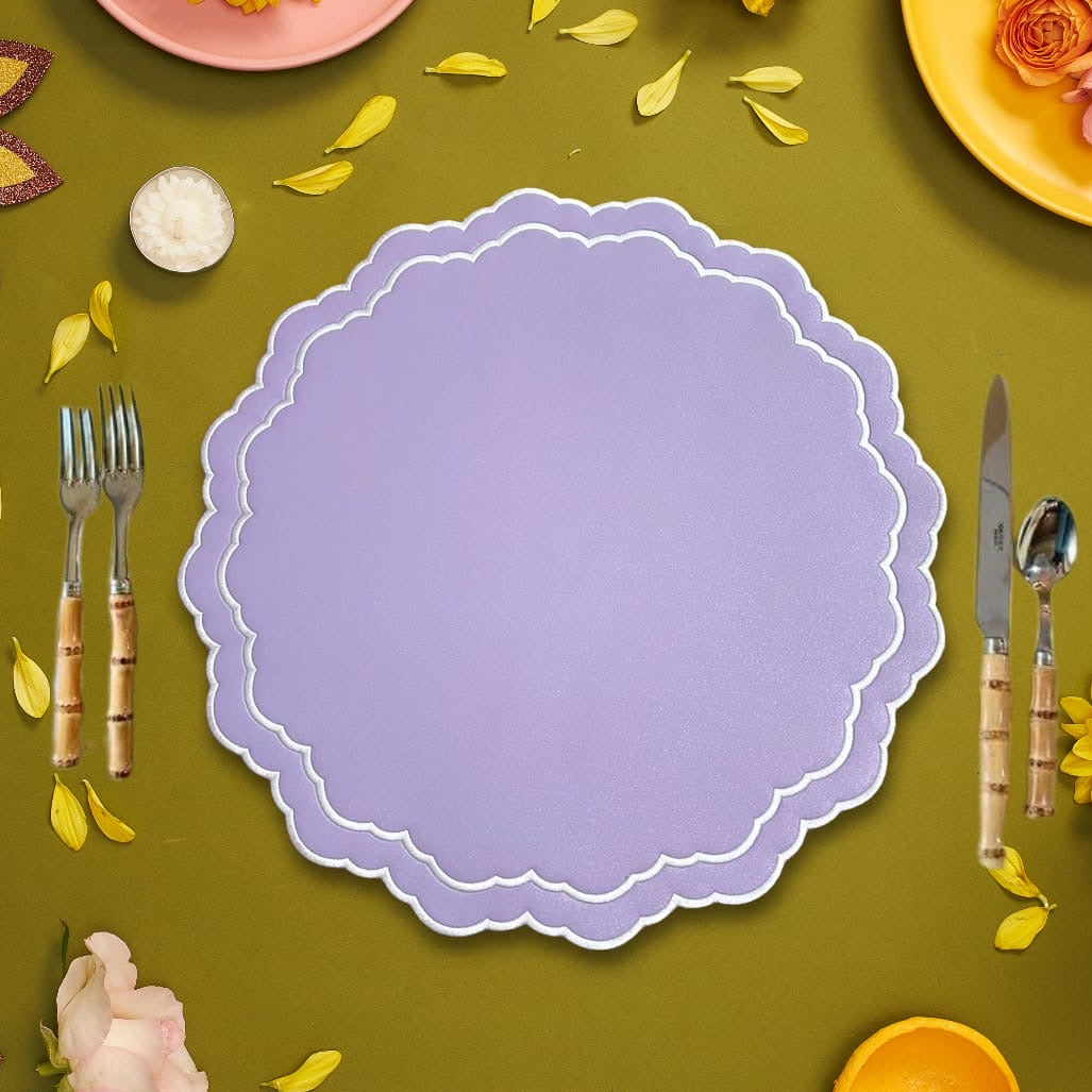 Purple scalloped placemat on a green surface with cutlery and decorative elements.