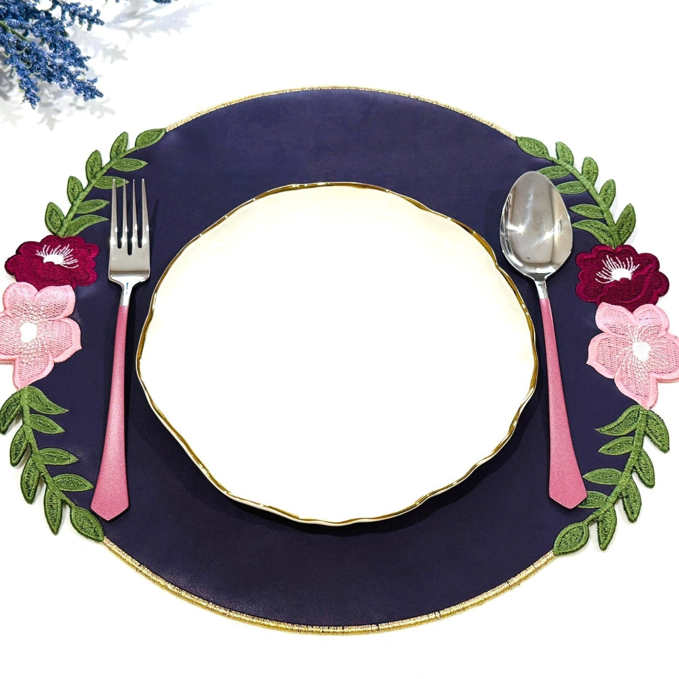 A purple faux leather placemat with decorative embroidery, presented on a white background with a fork, spoon, and a decorative floral arrangement.