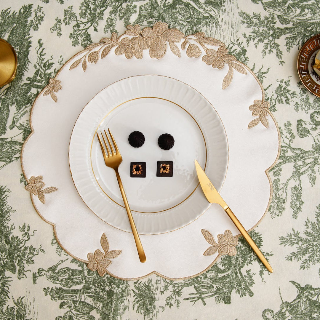 Table setting with white plates, gold cutlery, and decorative elements on a patterned tablecloth.