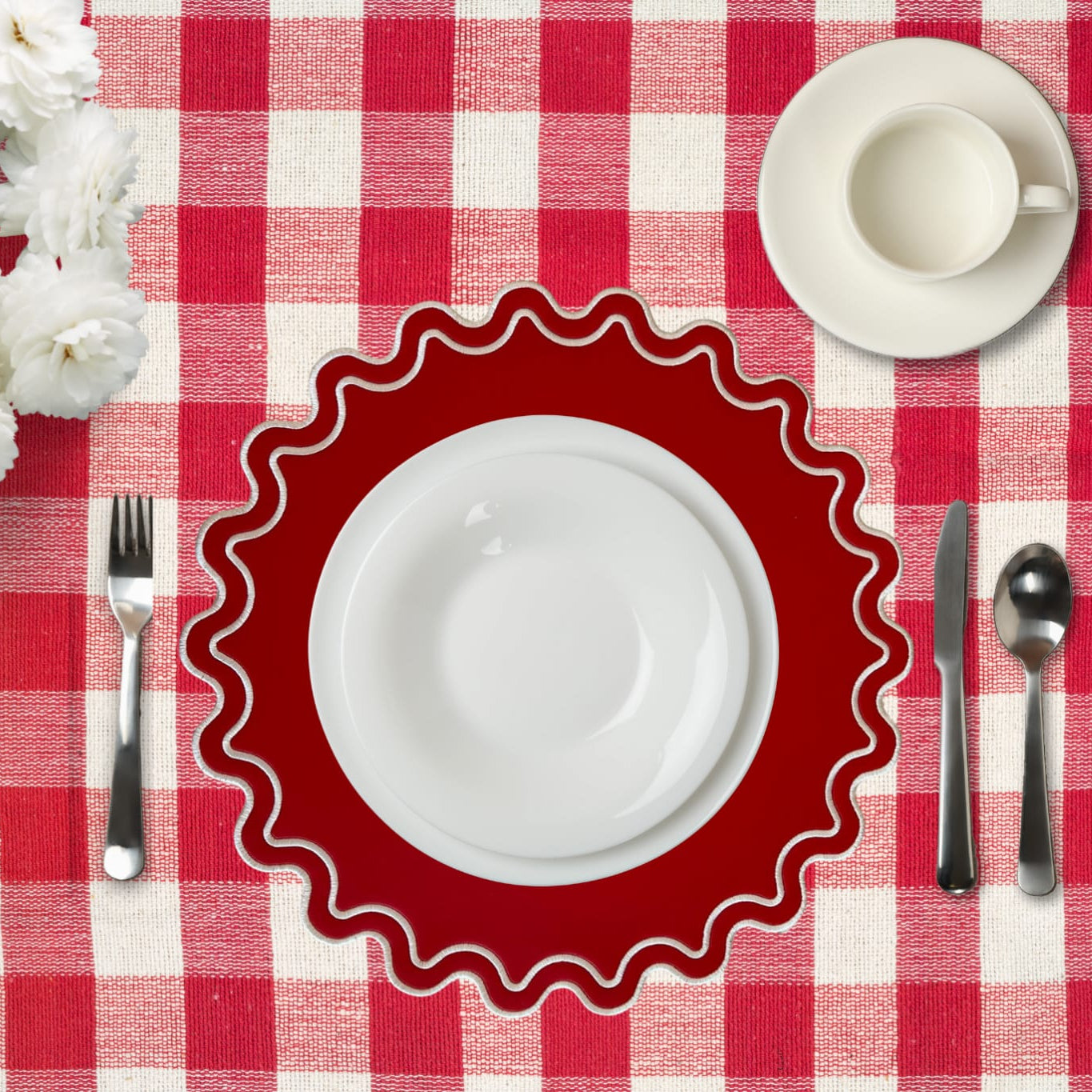 Red checkered tablecloth with a white plate, cup, and silverware on a red and white checkered tablecloth.