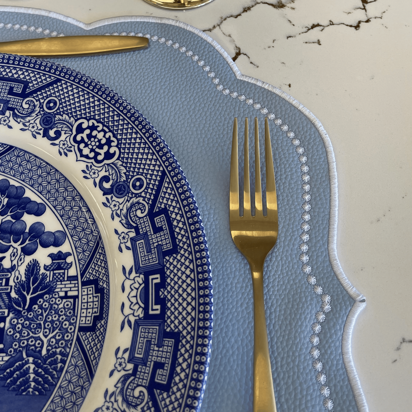 Table setting with blue and white plate, gold fork, and glass on a marble surface