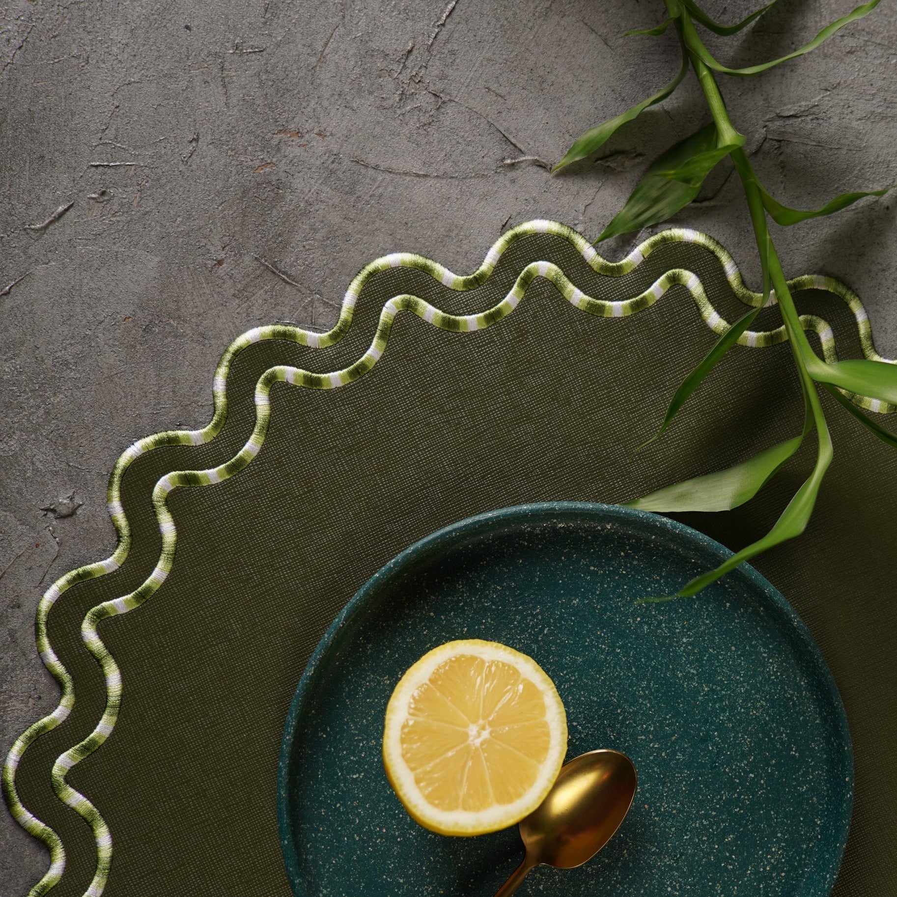 Green ceramic plate with a lemon slice and gold spoon on a textured surface