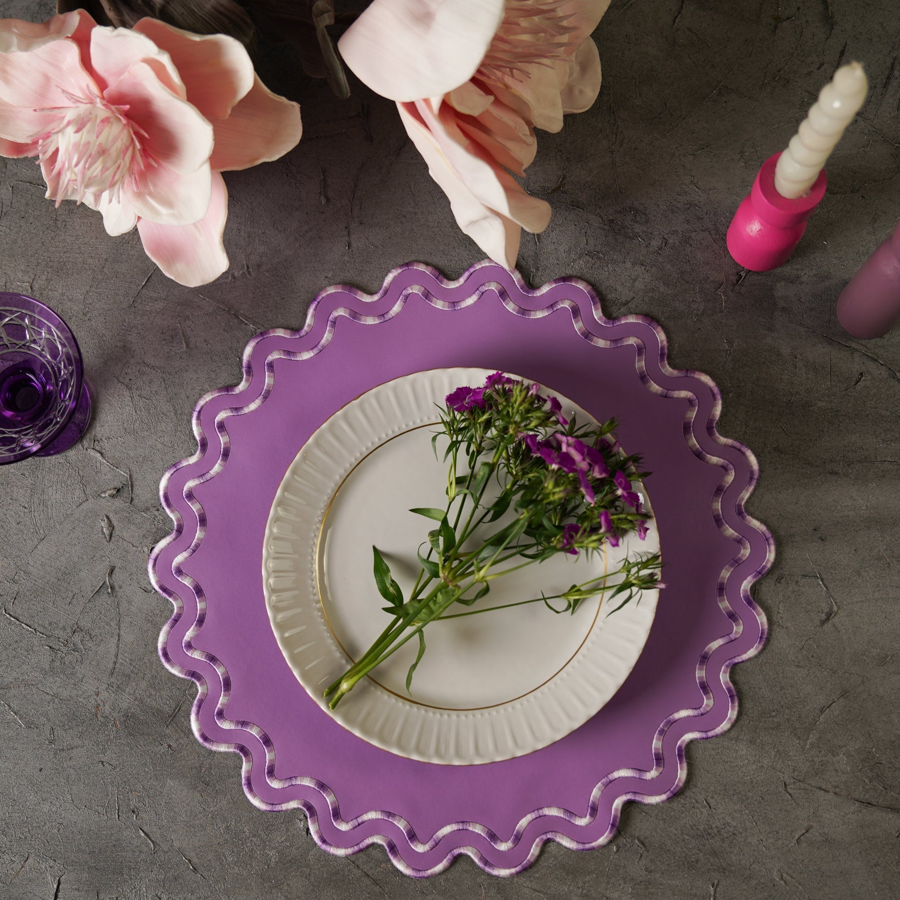 Purple decorative plate with a white plate featuring flowers on a gray surface.