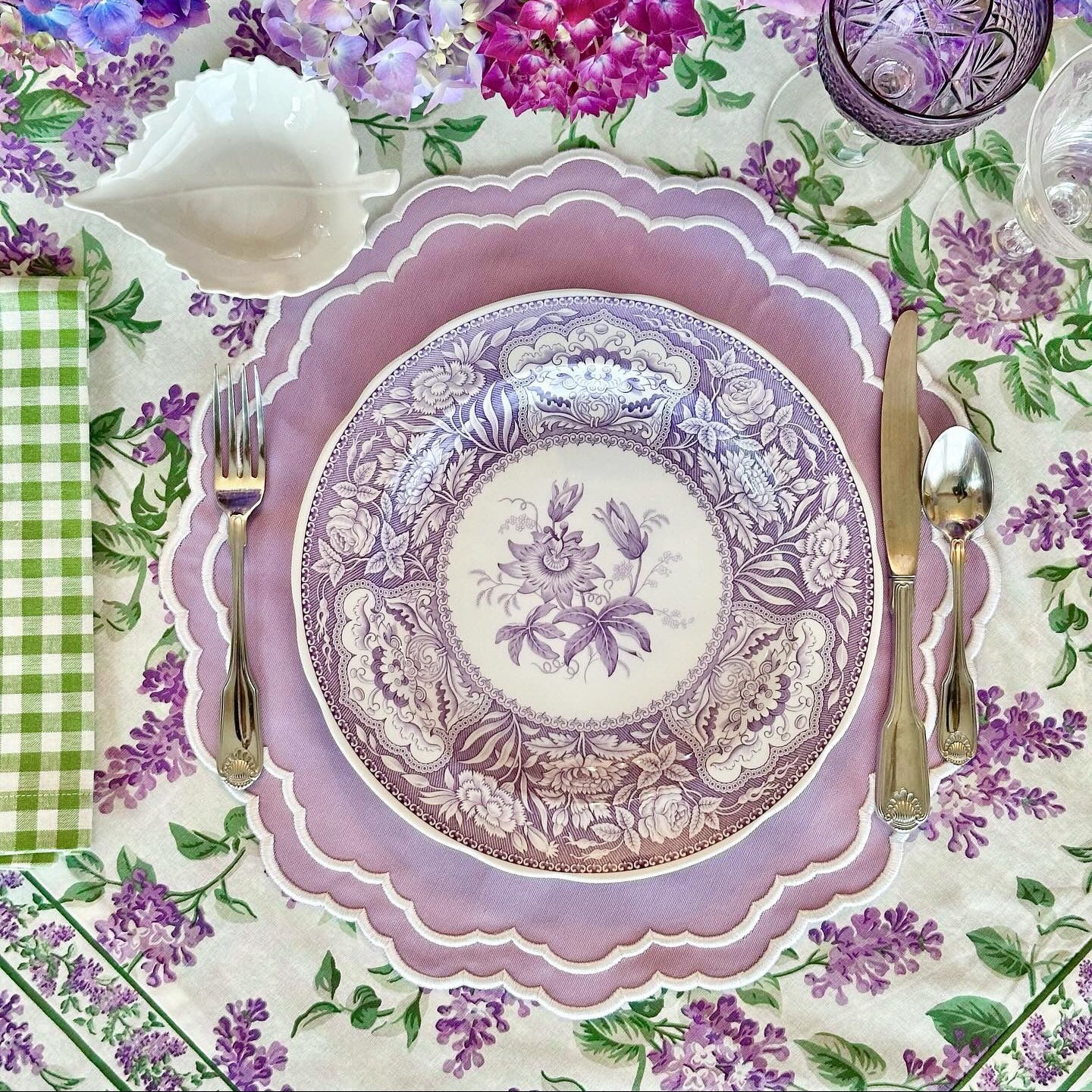 Decorative table setting with a purple plate, silverware, and floral tablecloth.