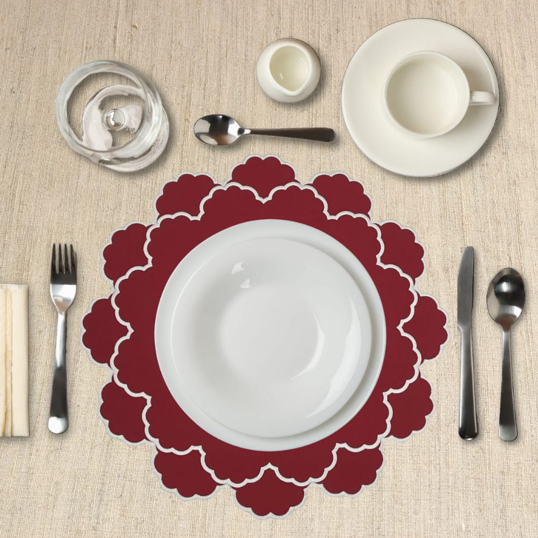 Table setting with a red placemat, white plate, and silverware on a beige tablecloth.