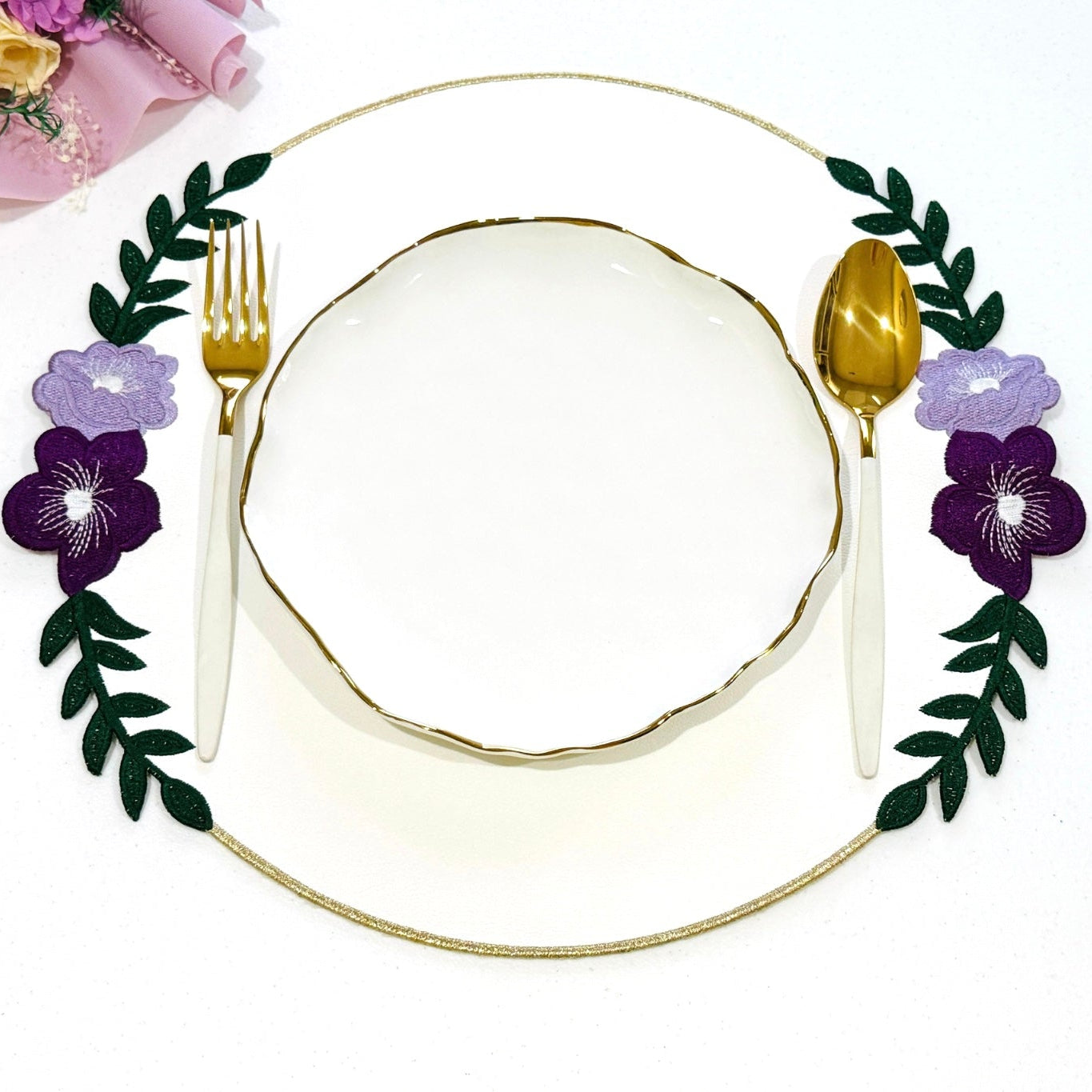 Decorative plate with gold rim, purple flowers, and green leaves on a white background