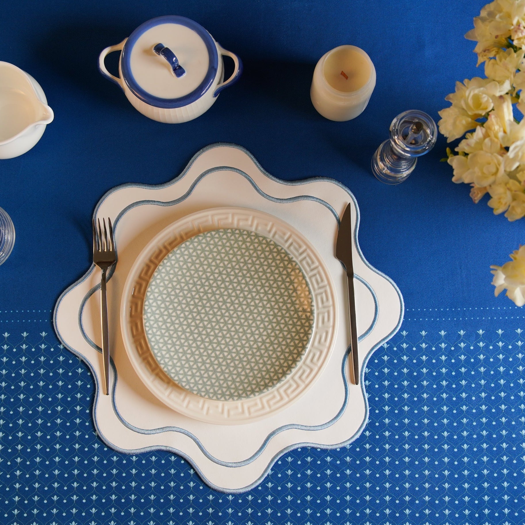 A blue faux leather placemat with a white floral pattern, displayed on a table setting with a plate, cutlery, and a vase.