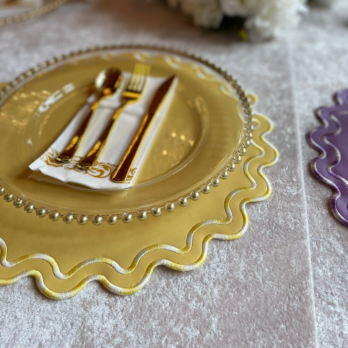 Gold plate with silverware on a decorative table setting with flowers.