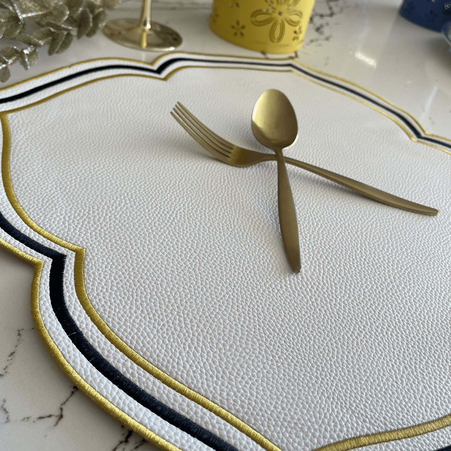 Gold fork and spoon on a decorative placemat with a yellow cup in the background.