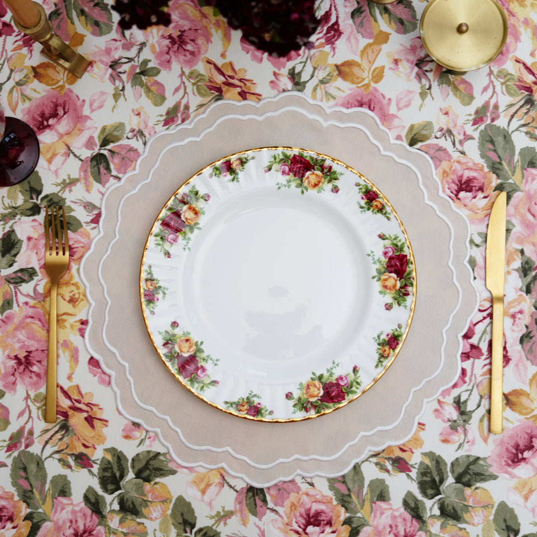 A set of elegantly embroidered placemats with a floral design in beige, white, and multicolor, displayed on a dining table with dishes and cutlery.