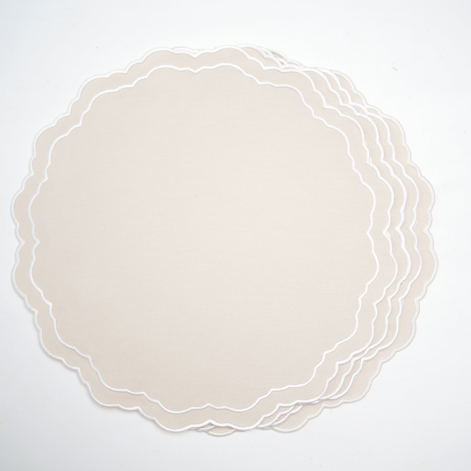 Set of round beige placemats with scalloped edge on a white background